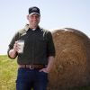 Kemps farmer smiling with a glass of milk next to a hay bail
