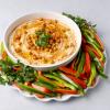 A bowl of hummus garnished with crispy roasted chickpeas and served on a platter with green and red bell pepper strips