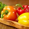 Red, orange, yellow and green bell peppers on a wooden cutting board